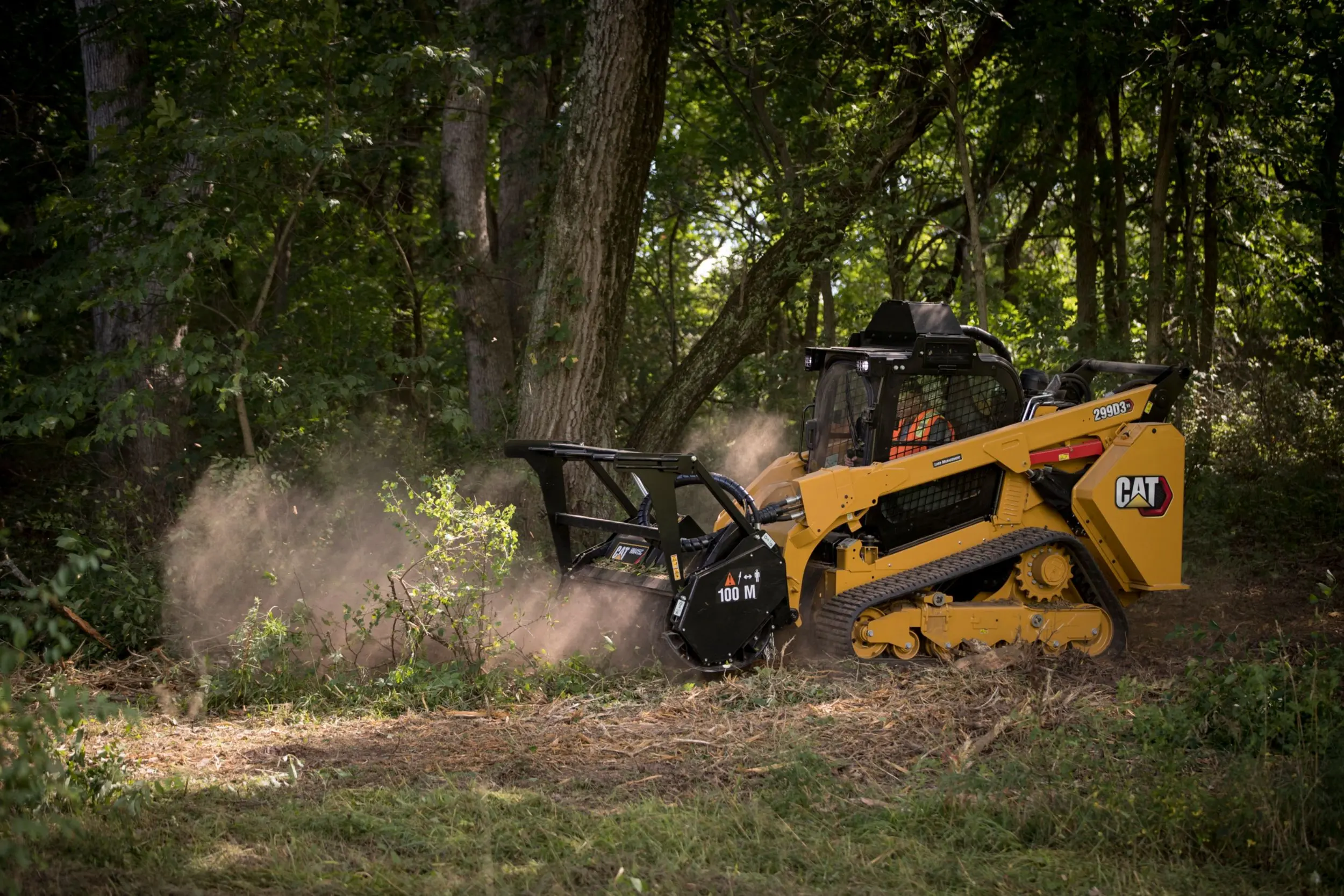 Cat compact track loader mulching dense brush along a wooded property edge