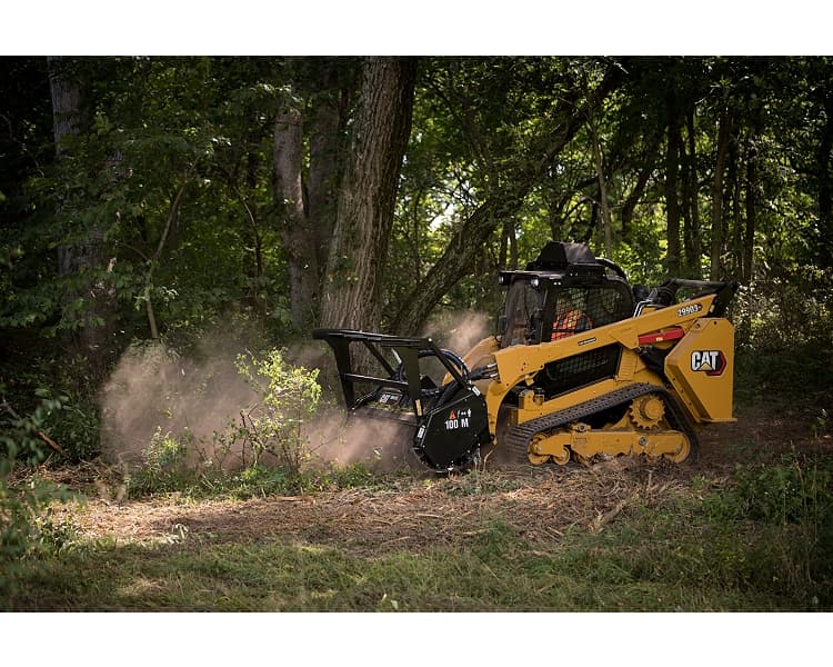 Cat compact track loader with forestry mulching head clearing brush at a wooded tree-line
